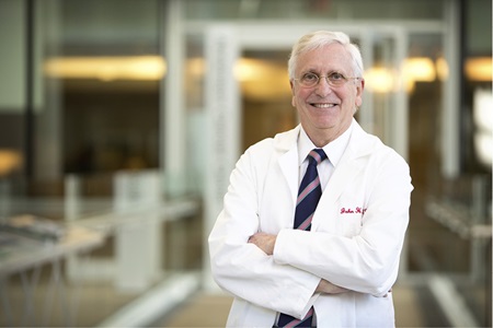 John Glick, MD, smiles while standing with his arms crossed, wearing a white coat